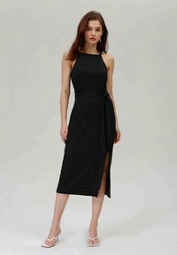Vestido midi preto com corpo ajustado, alças finas, fenda lateral e cintura com laço. Tecido texturizado com sutis adornos por toda a peça.