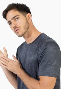 Grå kortærmet t-shirt med et tekstureret camouflage mønster og logoaccent. Lavet af letvægtsmateriale med rund halsudskæring.