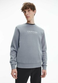 Sweatshirt grigio con collo a giro e logo ricamato in bianco. Polsini e orlo a coste, realizzato in morbido tessuto misto cotone.