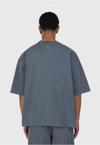 Grå oversized t-shirt lavet af bomuld med rund hals og korte ærmer. Glat tekstur, minimalistisk design og logo detalje på ryggen.