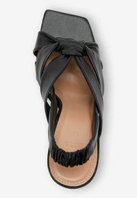 Černé kožené sandály se čtveratým špičkou a designem uzlu na popruhu. Má vycpanou stélku a na patě zdobení s nařasením.