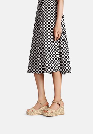 Sandali con zeppa e suola in juta intrecciata, con cinturini beige, abbinati a una gonna a quadri bianca e nera, che mette in mostra una silhouette aderente.