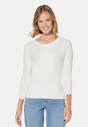 Weißer Pullover mit langen Ärmeln, der eine gerippte Textur, ein geometrisches Strickdesign auf den Schultern und einen runden Ausschnitt aufweist. Kombiniert mit hellblauen Jeans.