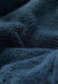 Dunkelblaues Fleece-Gewebe mit einer weichen, plüschigen Textur, das eine dichte, leicht strukturierte Oberfläche und subtile, unregelmäßige Muster aufweist.