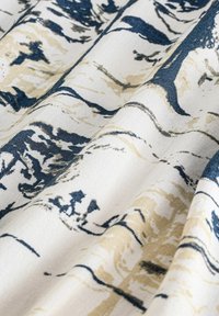 Tissu blanc avec des motifs abstraits marbrés bleus et beiges, présenté en gros plan sur des plis mettant en valeur la texture et les détails de l'impression.