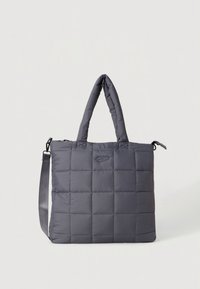 Sac cabas gris matelassé avec deux poignées et une bandoulière ajustable. Présente une texture lisse et un motif carré. Détail de branding minimaliste.