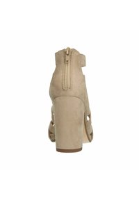 Beige suède sandaal met hak, voorzien van een achterrits, open hiel en een criss-cross band ontwerp. De hak is chunky en heeft een textuur voor stabiliteit.
