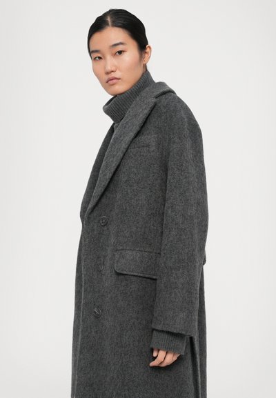 Manteau en laine grise avec un col cranté, design à double boutonnage et poches latérales, associé à un pull à col roulé côtelé.