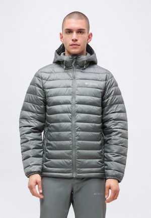 Homme portant une veste matelassée grise Columbia avec capuche et un pantalon gris assorti, face à l'avant sur un fond uni.