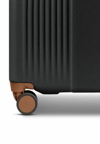 Valigia rigida di colore nero opaco con righe verticali e un accento marrone sulla base. Presenta una ruota resistente per la mobilità.
