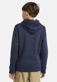 Námornícky modrá mikina s kapucňou vyrobená zo zmesi bavlny, s kloktacou vreckom a rebrovanými manžetami a spodným lemom, zobrazená zozadu.