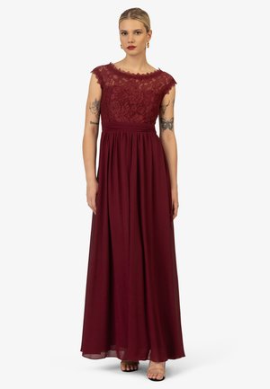 Lungo vestito da sera bordeaux con corpetto in pizzo, maniche a cappuccio, vita arricciata e gonna in chiffon fluida. Semplici tacchi con cinturino alla caviglia completano il look.