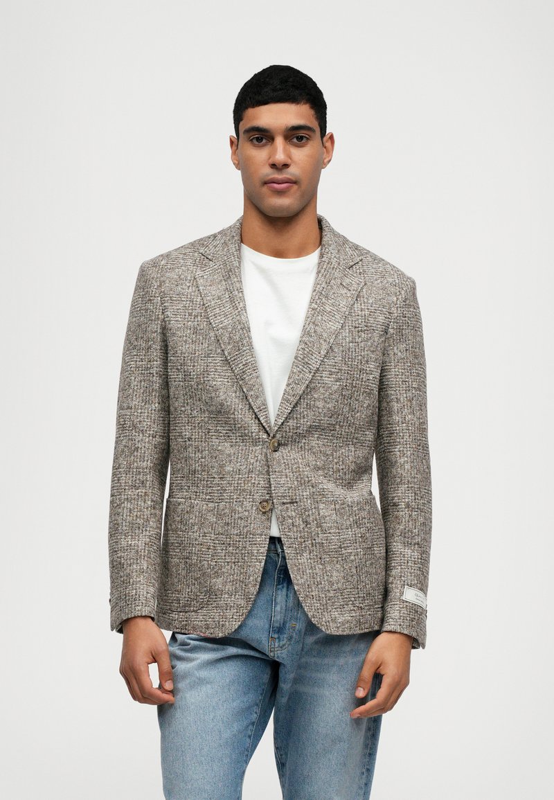 Bruine textuur blazer met een notched lapel, enkele knoopsluiting en zijzakken, gedragen over een wit shirt en jeans.