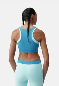 Sutien sportiv albastru cu accente albastre deschise și un design fără cusături. Poartă cu colanți asortați în bleu deschis, evidențiind un fit confortabil.