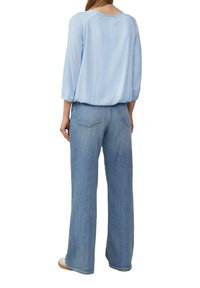 Himmelblaues, langärmliges Blusenshirt mit gerafftem Rückendetail, kombiniert mit hellblauen, weit geschnittenen Jeans mit zwei hinteren Taschen und einem verblassten Look.