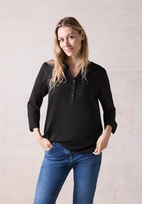 Sort, langærmet bluse til kvinder med V-udskæring og knappet front. Kombineret med blå jeans, hvilket giver et afslappet look.