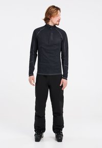 Maglia a maniche lunghe nera con zip a metà e cuciture grigie a contrasto, dal taglio slim, abbinata a pantaloni da sci neri e stivali.