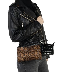 Person iført sort læderjakke og grå jeans holder to crossbody-tasker: en med leopardprint og en sort skinnende quiltet.