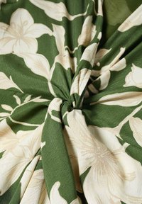 Tissu vert torsadé au centre avec un grand motif floral crème, montrant la texture et les plis.