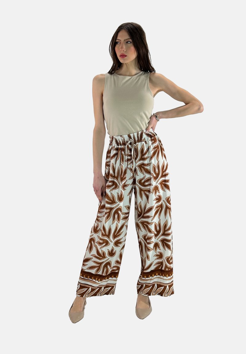 Beige mouwloze top in combinatie met witte, wijdvallende broek met een bruin blaadjespatroon en een strikband in de taille.