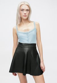 Ανοιχτό μπλε ριχτό τοπ με κουμπί, συνδυασμένο με φαρδύ μαύρο δερμάτινο φούστα. Λείες υφές και αντίθετα χρώματα.