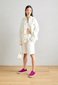 Giacca di denim bianco e pantaloncini abbinati a una maglietta bianca, completati da sneakers in suede viola e una piccola borsa bianca.