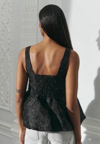 Must mustriga mustriga tops, mille tugevade õlgadega ja smockitud seljaga. Läikivad aktsendid lisavad detaili.