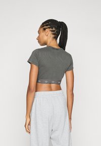 Šedý žebrovaný krátký top s krátkými rukávy, se subtilním logem podél lemu, nošený s světle šedými tepláky.