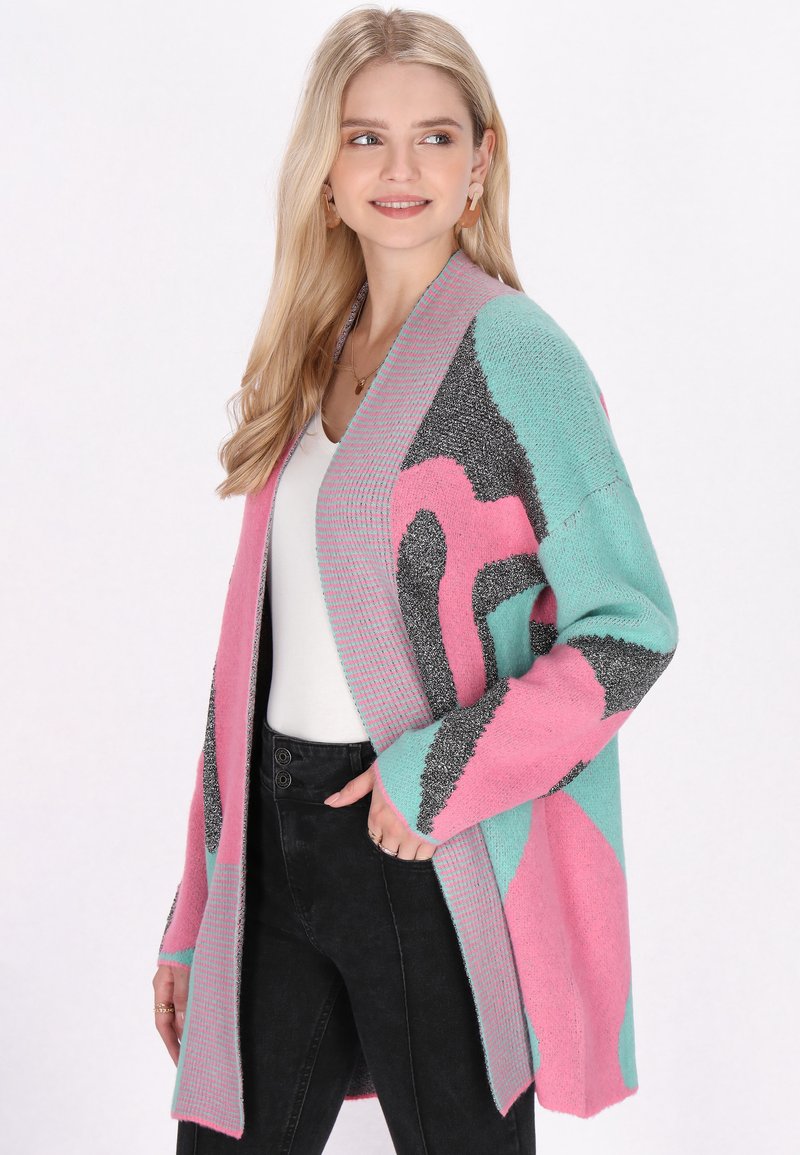 Cardigan colorato con motivi rosa, teal e grigio, dalla texture morbida, design aperto e bordi a costine, indossato su una maglietta bianca.