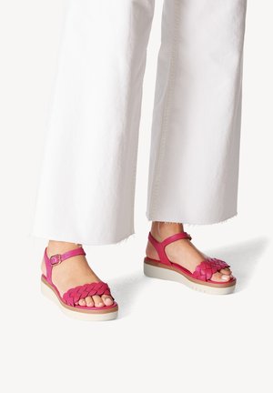 Sandali intrecciati fucsia con un design testurizzato, cinturino alla caviglia regolabile e una suola in platform di colore chiaro, abbinati a pantaloni bianchi a gamba larga.