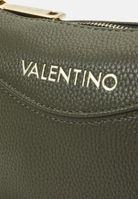 Zelená texturovaná kožená kabelka se zlatým logem "Valentino"; obsahuje úzký zip a jemné detaily stehu.
