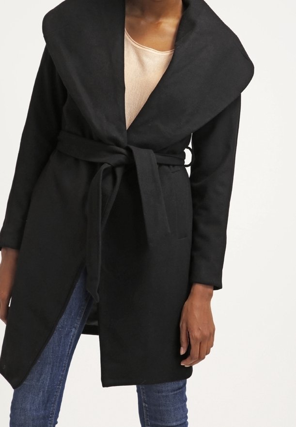 Cappotto nero avvolgente con colletto oversize, cintura in vita, maniche lunghe e texture morbida, abbinato a una maglietta leggera e jeans blu.