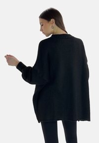 Maglione oversize nero realizzato in materiale a maglia testurizzata, con colletto alto e maniche larghe. L'orlo è leggermente sfilacciato.