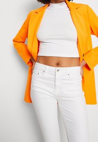 Orange kavaj, vit kort topp och vita jeans. Slät tyg, skräddarsydd design, slim fit och minimala detaljer i metall.