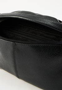 Μαύρη τσάντα από ψεύτικο δέρμα με υφή, με άνοιγμα με φερμουάρ και επένδυση στο εσωτερικό. Περιλαμβάνει μια μικρή εσωτερική τσέπη με φερμουάρ.