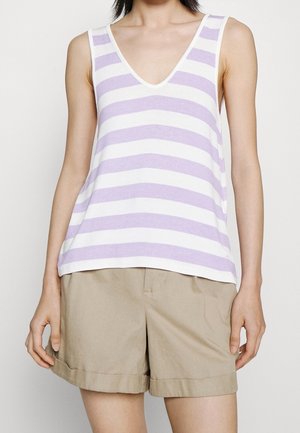 Woman wearing sleeveless white and lavender striped V-neck top tucked out over beige cuffed shorts.