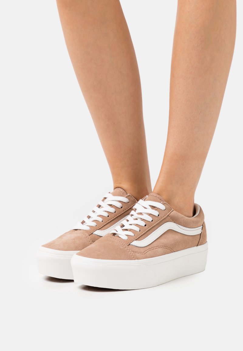 Baskets compensées en daim marron clair avec lacets blancs et bande latérale blanche portées pieds nus sur un fond uni.