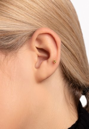 Orecchino a perno in oro posizionato sul lobo dell'orecchio, forma rotonda, superficie liscia, design minimalista, valorizzato da capelli biondo chiaro.