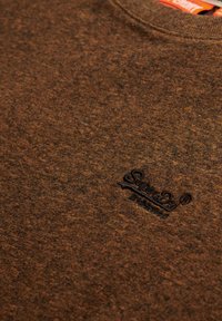 Camisa de manga larga marrón mélange hecha de un tejido suave, con un cuello redondo y un logo bordado en negro en el lado izquierdo del pecho.