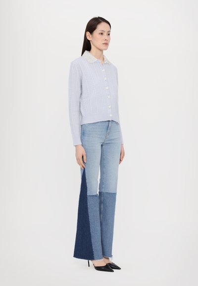 Cardigan di maglia a treccia blu chiaro con bottoni di perla, abbinato a jeans a zampa d'elefante in denim patchwork in varie tonalità di blu e tacchi a punta neri.