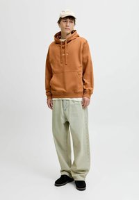 Brun huoodad sweatshirt med dragsko och framficka, parat med lösa ljusblå jeans och svarta skor. Beiget keps fulländar outfiten.