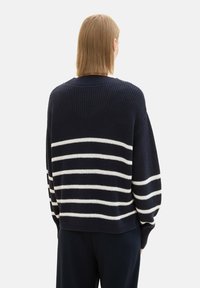 Marineblauer Strickpullover mit weißen horizontalen Streifen, oversized Schnitt, Rippstricktextur und rundem Ausschnitt. Rückenansicht, die das Design und den Farbkontrast zeigt.