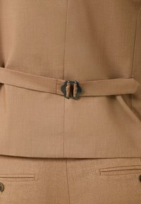 Veste de costume marron clair avec ceinture en tissu réglable et boucle métallique noire à la taille, associée à un pantalon texturé assorti.