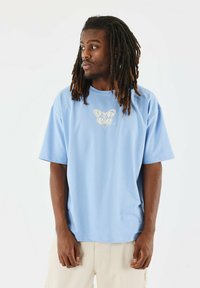 Camiseta de manga corta azul claro con un corte holgado, que presenta un gráfico de mariposa color crema en el pecho. Hecha de un material de algodón suave.