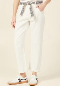 Pantaloni in denim bianco con una cintura in tessuto a fantasia, caratterizzati da una vestibilità ampia e orli risvoltati. Abbinati a sneakers grigie e bianche con dettagli neri.