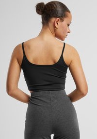 Black crop top with thin straps, smooth texture, paired with grey ribbed high-waisted pants, displayed from the back.