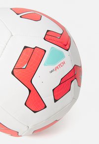 Fotbal Nike Pitch, převážně bílý s červenými geometrickými vzory. Má hladký povrch, lesklý finiš a kontrastní tyrkysov�é akcenty.