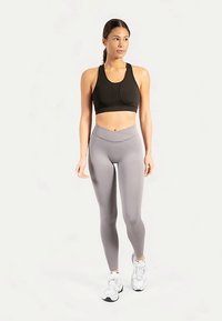 Zwarte sportbeha en lichtgrijze leggings met hoge taille, beide gemaakt van rekbaar materiaal. Sneakers zijn wit met grijze accenten.