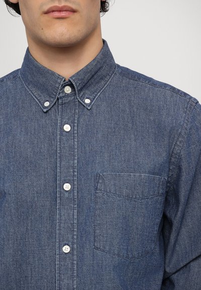 Camicia in denim blu scuro con collo a punta, dotata di bottoni bianchi, una tasca sul petto e una superficie di tessuto texturizzato.