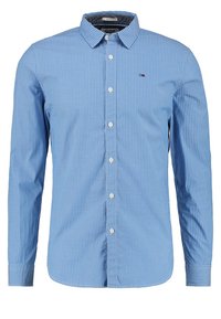 Modrá košile s knoflíky, vertikální bílé pruhy, dlouhé rukávy, límeček a bílé knoflíky. Obsahuje malé logo na levé části hrudi.